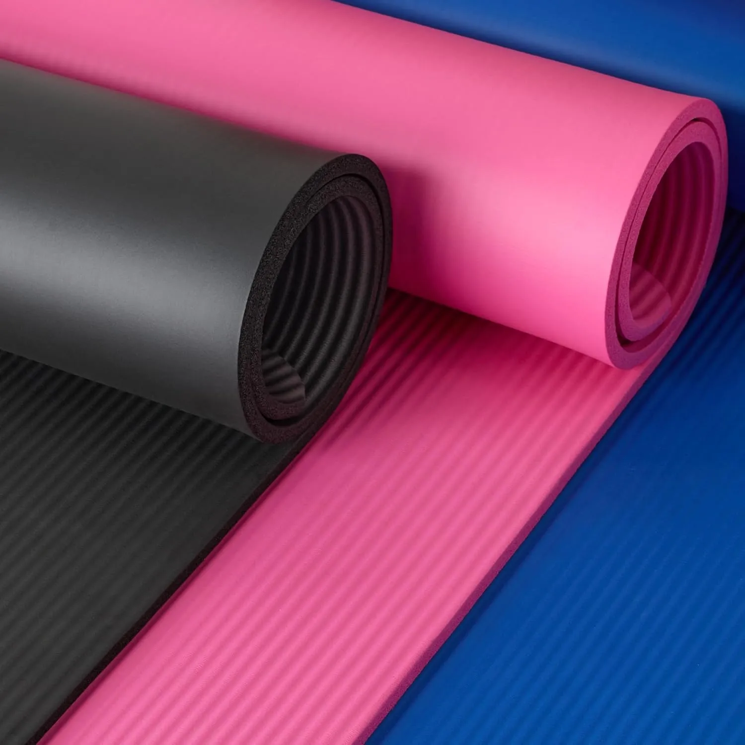 Rolled exercise mats in black, pink, and blue showing foam texture.