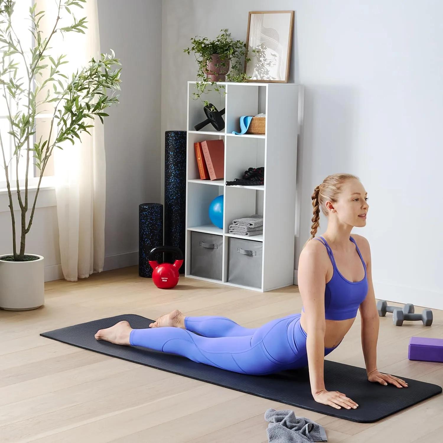 Man carrying a rolled black Amazon Basics exercise mat with strap in a home workout room.